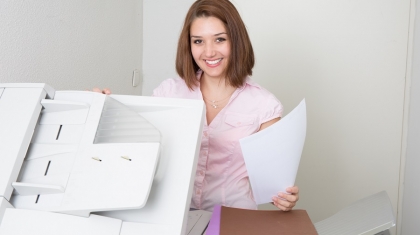 Smiling business woman operating photocopy machine in office