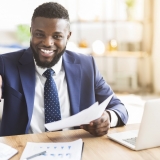 Partnership concept. Smiling young african american businessman holding documents and extending hand to shake, office interior, copy space